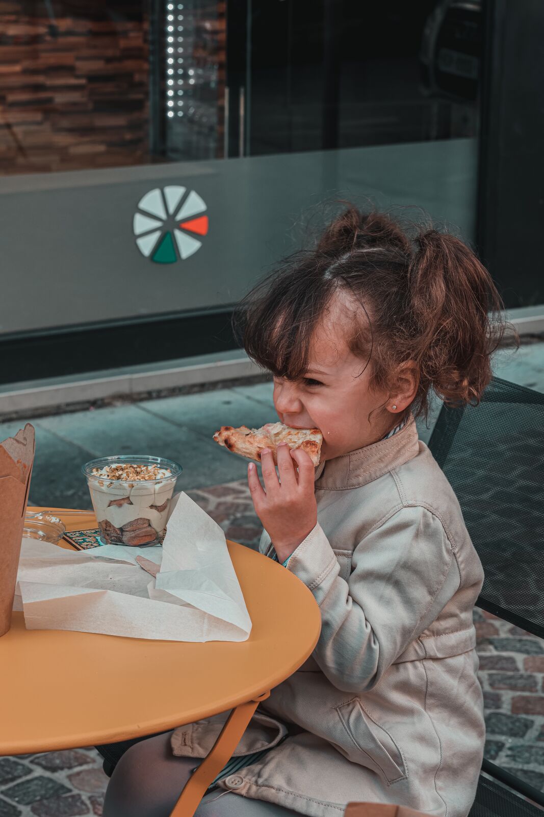 Une enfant croque une part de pizza devant la vitrine Bellini